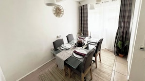 Un coin repas avec une table dressée pour quatre personnes, une horloge au mur et une fenêtre avec des rideaux.
