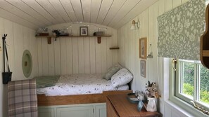 Et hyggeligt soveværelse med seng, et lille bord, et vindue med udsigt og en hylde med pynt.