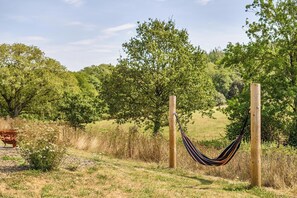 A hammock tied between two wooden posts in a grassy field with trees in the background.