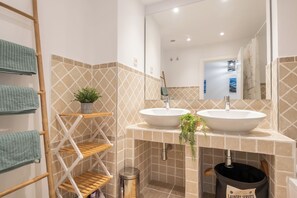 A bathroom with two sinks, a mirror, a towel rack, and a trash can.