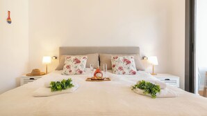 Un lit bien fait, agrémenté d’oreillers à motifs floraux, de lampes de chevet et d’un plateau sur lequel se trouvent une bouteille et des verres.