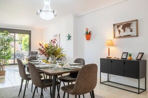A dining area with a table set for four, surrounded by chairs, a chandelier, a potted plant, and a cabinet with decorative items.