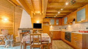 Interior de una cabaña de madera con comedor, cocina y televisor.