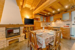 A wooden interior with a dining table set for four, a fireplace, and a kitchen area with cabinets and a TV.