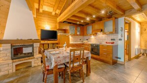 Interior de una cabaña de madera con chimenea, mesa de comedor y zona de cocina.