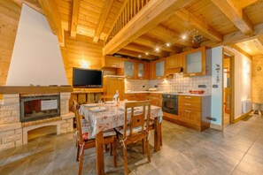 A wooden cabin interior with a fireplace, dining table, and kitchen area.