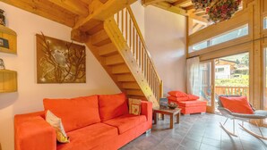 Una sala de estar con una escalera de madera, un sofá rojo, un sillón mecedor y un cuadro de un búho.