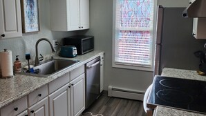 A kitchen with white cabinets, a stainless steel sink, a microwave, and a refrigerator. - Hale Ali'i (Anchorage)