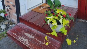A front door with a 'WELCOME' sign, a mailbox, a hanging lantern, and a potted plant with flowers. - Hale Ali'i (Anchorage)