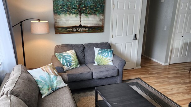 A living room with a gray sofa, a coffee table, and a painting of a tree on the wall. - Hale Ali'i (Anchorage)