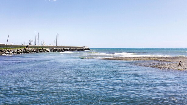 A beach with a rocky breakwater, calm sea, and a person walking on the shore. - 2 bedroom lovely home in Ne (Ne)