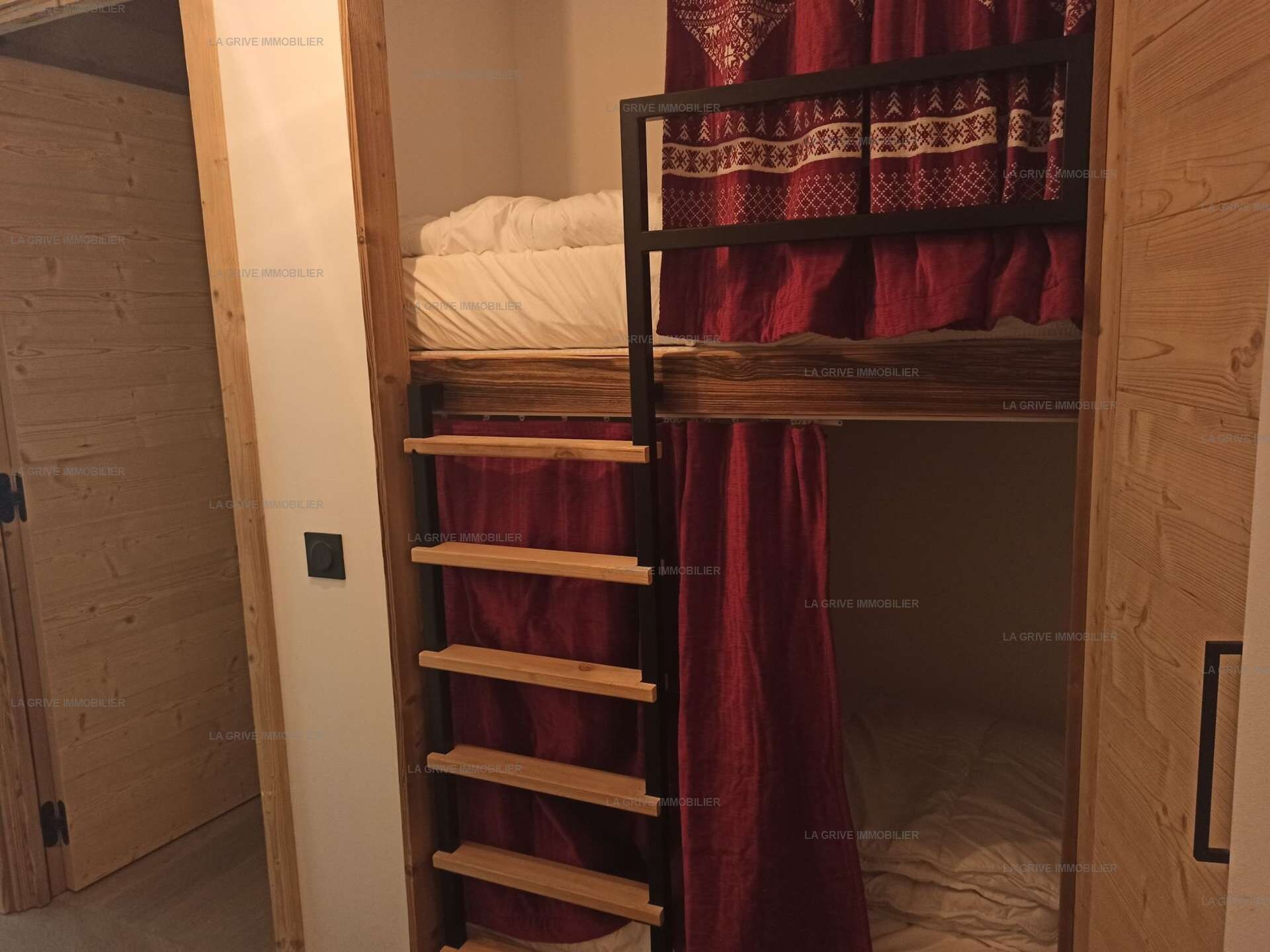 A room with a bunk bed, a wooden ladder, and a red curtain.