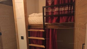 Una habitación con una cama litera, una escalera de madera y una cortina roja.