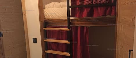 Une chambre avec un lit superposé, une échelle en bois et un rideau rouge.