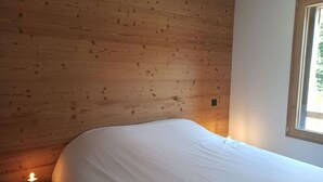 Ein Schlafzimmer mit Holz-Kopfstütze, einem Bett mit weißer Bettwäsche, einem Nachttisch mit Lampe und einem Fenster mit Blick ins Grüne.