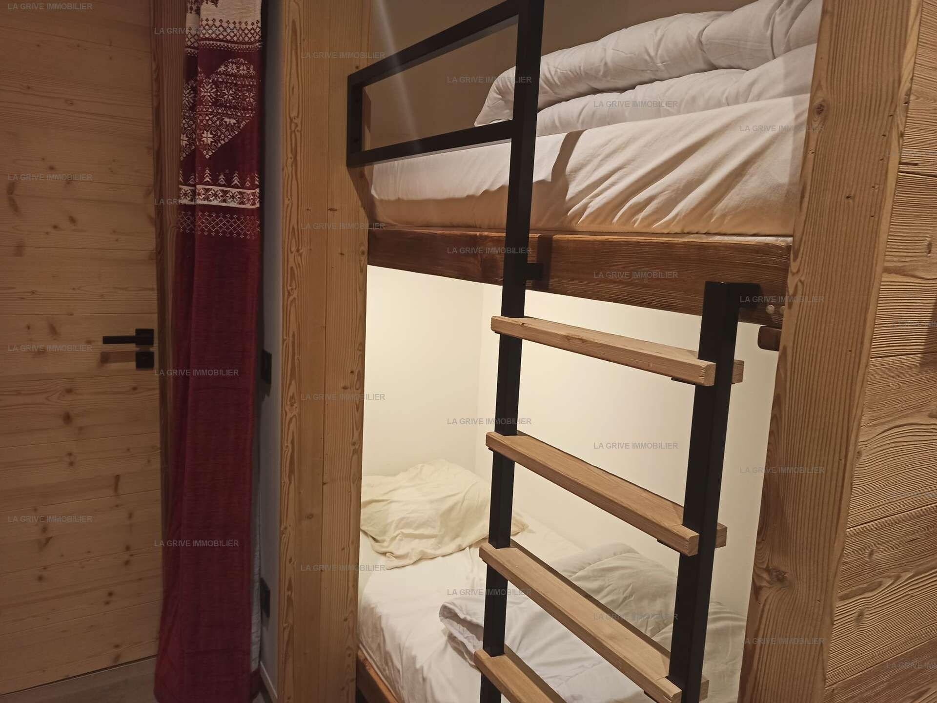 A bunk bed with a ladder, wooden walls, and a patterned curtain.