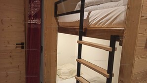 Una cama litera con escalera, paredes de madera y una cortina estampada.