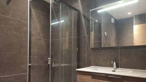 Un baño moderno con cabina de ducha de vidrio, tocador de madera y un espejo grande.
