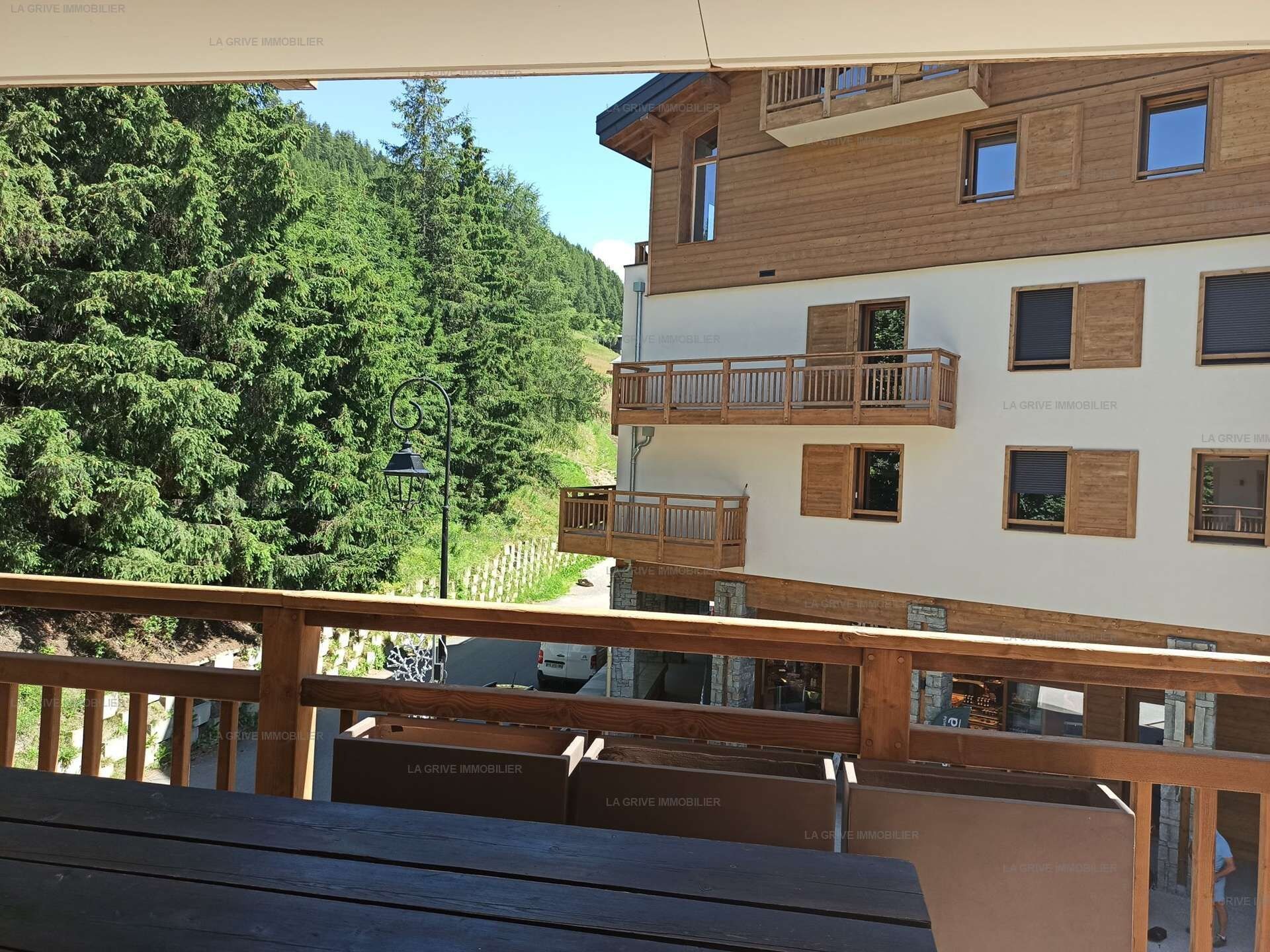 A multi-story building with balconies, a wooden deck, and a forested hillside in the background.