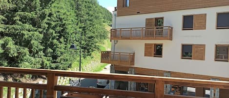 A multi-story building with balconies, a wooden deck, and a forested hillside in the background.