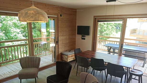 Amplia sala de estar con una terraza de madera, una mesa de comedor con sillas y un televisor montado en la pared.
