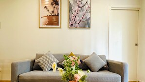 A living room with a grey sofa, a wooden coffee table, and a vase with flowers. There are two framed pictures on the wall.