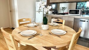 A dining table set with white plates, wine glasses, and cutlery, surrounded by wooden chairs.