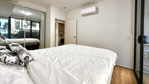 A bedroom with a large bed, a mirror, and an air conditioning unit on the wall.