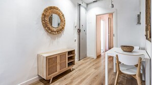 A modern interior with a wooden cabinet, a round mirror, and a white table with a basket. - MEDITERRANEO 2 APARTMENT (Barcelona)
