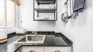 A modern kitchen with a black countertop, a stainless steel sink, and a wall-mounted shelf with dishes and glasses. - MEDITERRANEO 2 APARTMENT (Barcelona)
