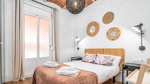 A bedroom with a bed, bedside tables, a lamp, and a window with curtains. - MEDITERRANEO 2 APARTMENT (Barcelona)