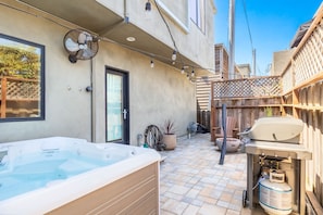 Ein Garten mit Whirlpool, Grill und einer Terrassenfläche.