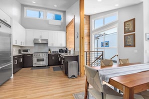 A modern kitchen with stainless steel appliances, dark cabinets, and a wooden dining table with chairs. - 4 Bedroom Luxury in Capitola Village w/ parking! (Capitola)