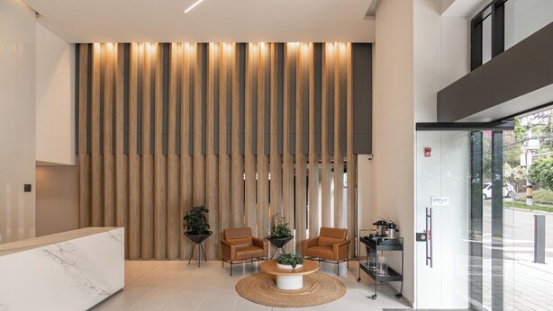 Un área de recepción moderna con un mostrador de mármol, dos sillones de cuero, una mesa de centro redonda y un panel de pared de madera.