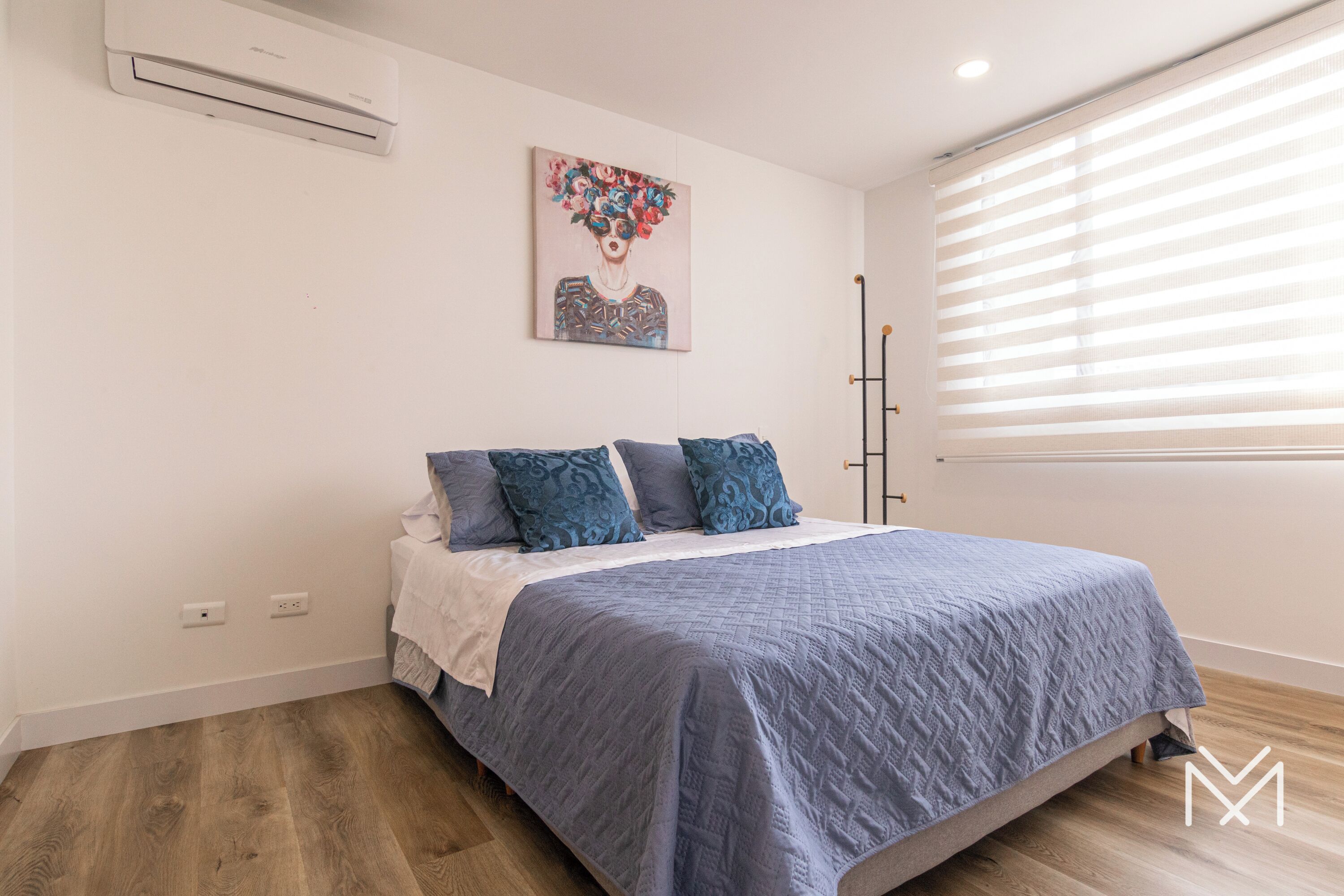 Un dormitorio con cama, un cuadro en la pared y una ventana con persianas.