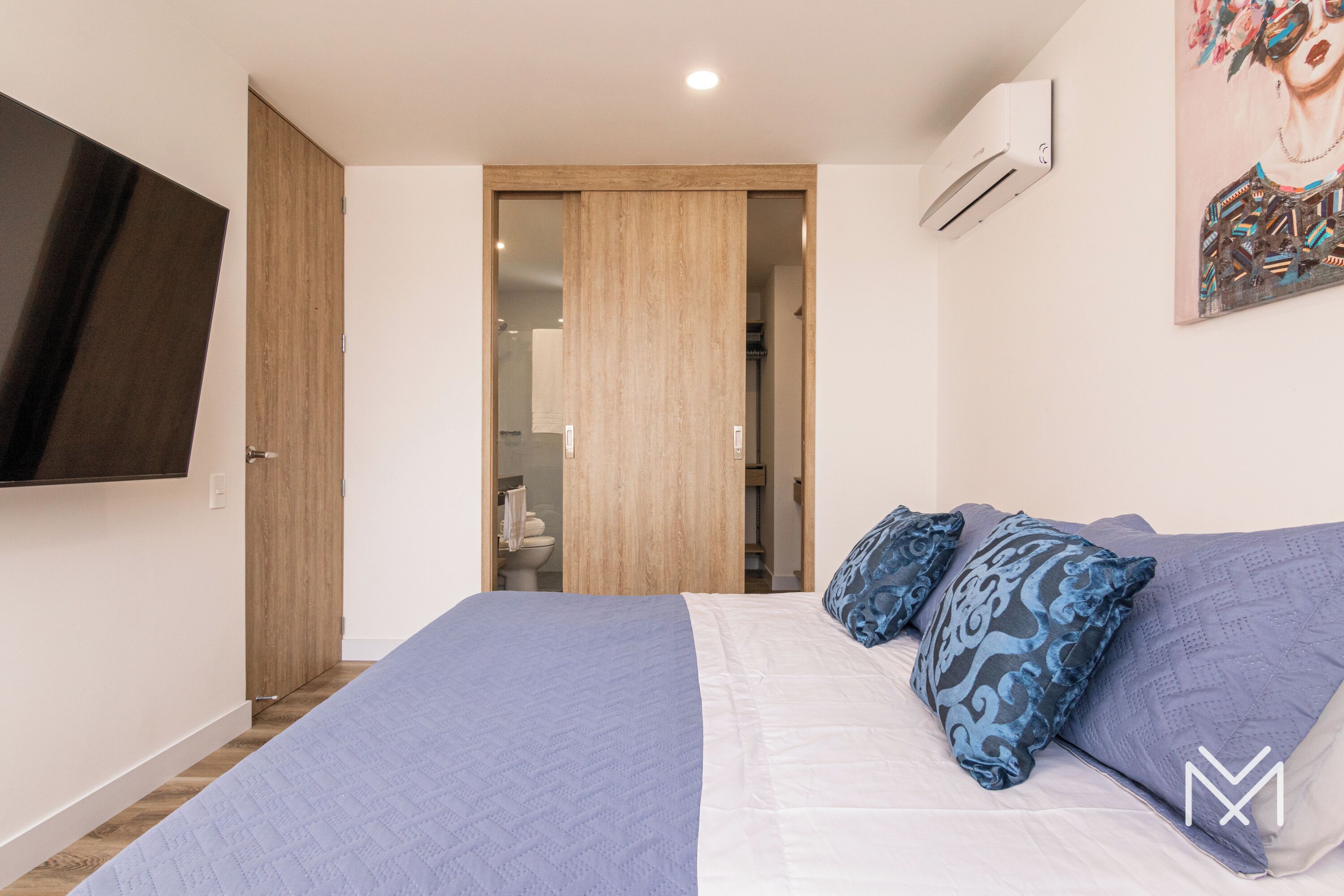 A bedroom with a bed, a TV mounted on the wall, and a door leading to a bathroom.