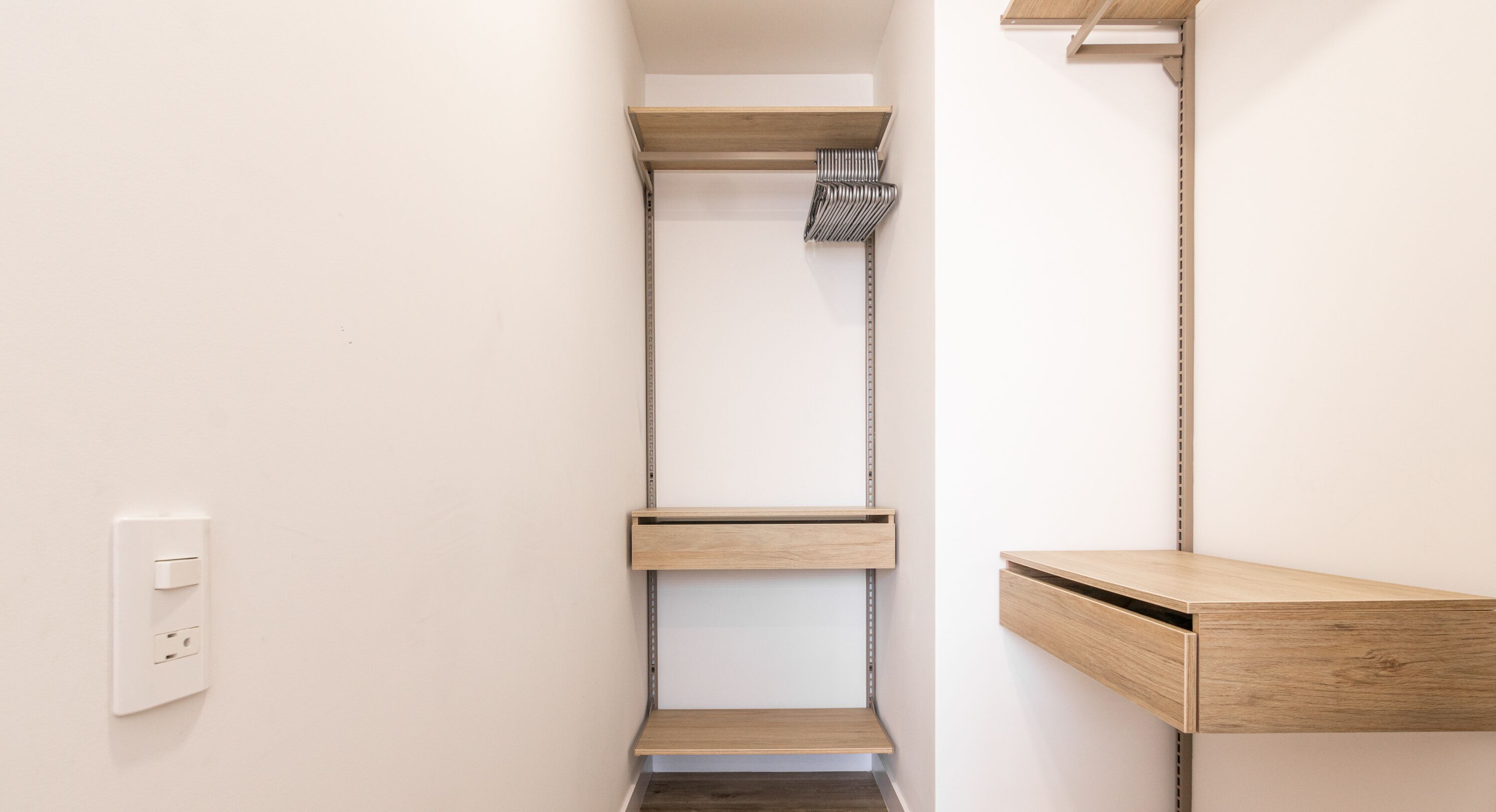 A narrow bathroom with a built-in shower, a wooden shelf, and a small wooden cabinet.