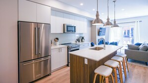 A modern kitchen with stainless steel appliances, a wooden island with stools, and a large window offering a view of the city.