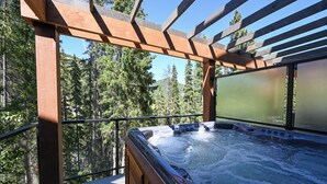 A hot tub with a wooden pergola and a view of a forested area.
