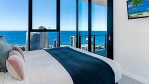 Une chambre avec une grande fenêtre donnant sur l’océan et le panorama urbain.