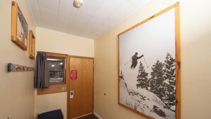 A hallway with a wooden bench, a door with a red sign, and a large framed picture of a skier on a snowy mountain. - Yodeler Motel (Red Lodge)