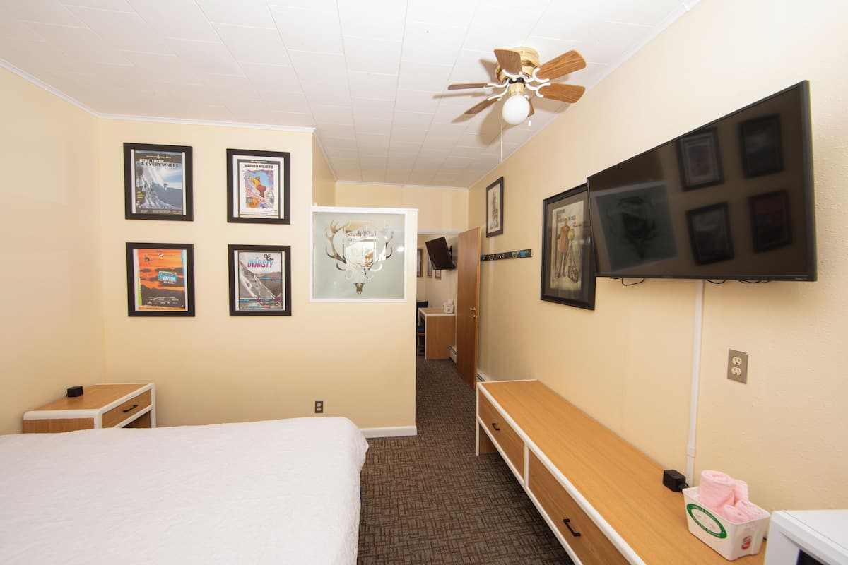 A hotel room with a bed, a TV, a ceiling fan, and framed pictures on the wall.