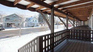 A covered wooden deck with a railing, a snow-covered ground, and houses in the background. - Yodeler Motel (Red Lodge)