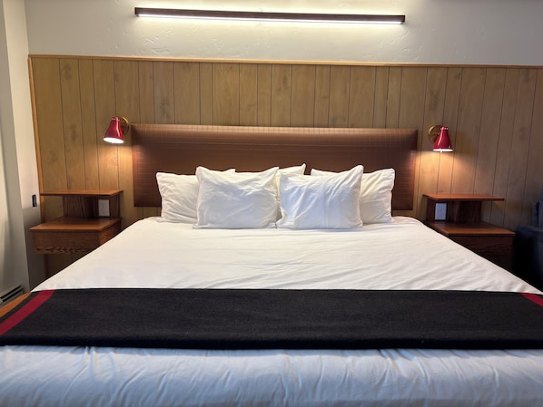 Una habitación de hotel con cabecera de madera, ropa de cama blanca y dos lámparas de noche.