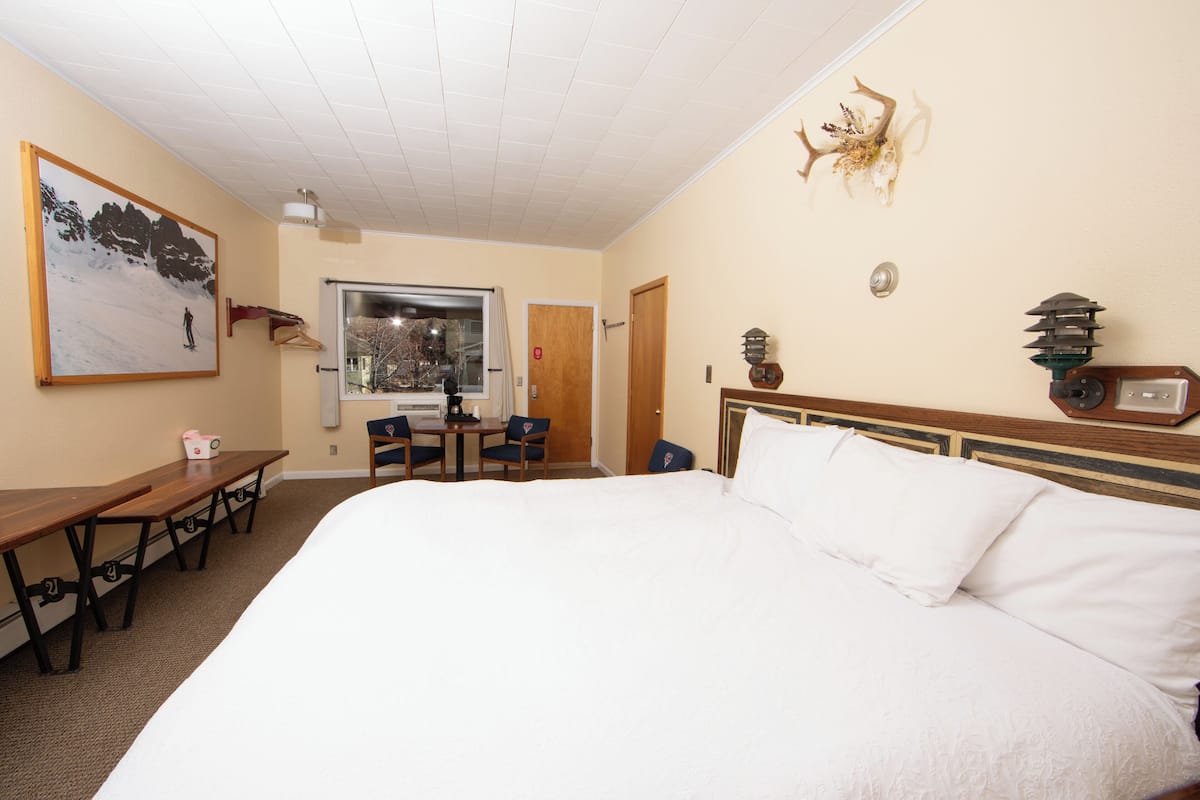 A hotel room with a large bed, a desk with chairs, a window, and a door.