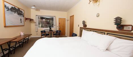 A hotel room with a large bed, a desk with chairs, a window, and a door.