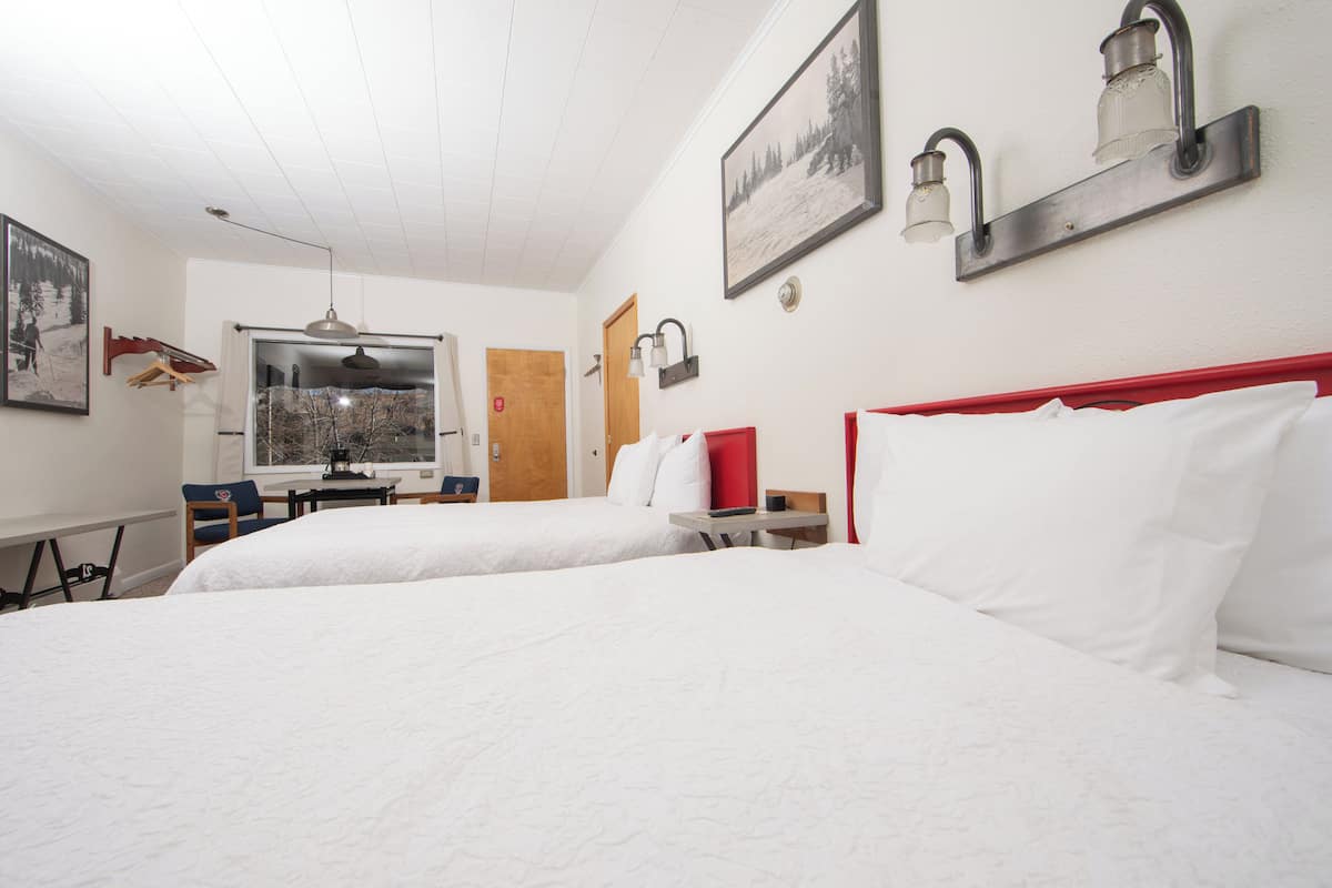 A hotel room with two beds, a desk, a chair, and a window with a view.