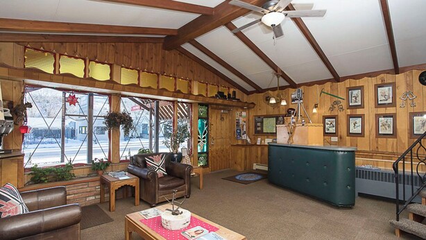 A cozy, rustic interior with wooden walls, a ceiling fan, a reception desk, and a seating area with a coffee table. - Yodeler Motel (Red Lodge)