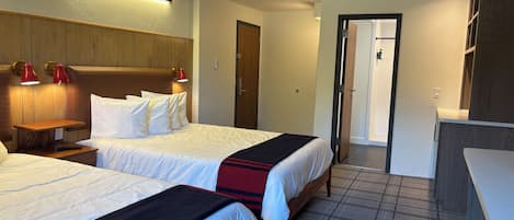 A hotel room with two beds, a wooden headboard, a nightstand, and a red lamp.