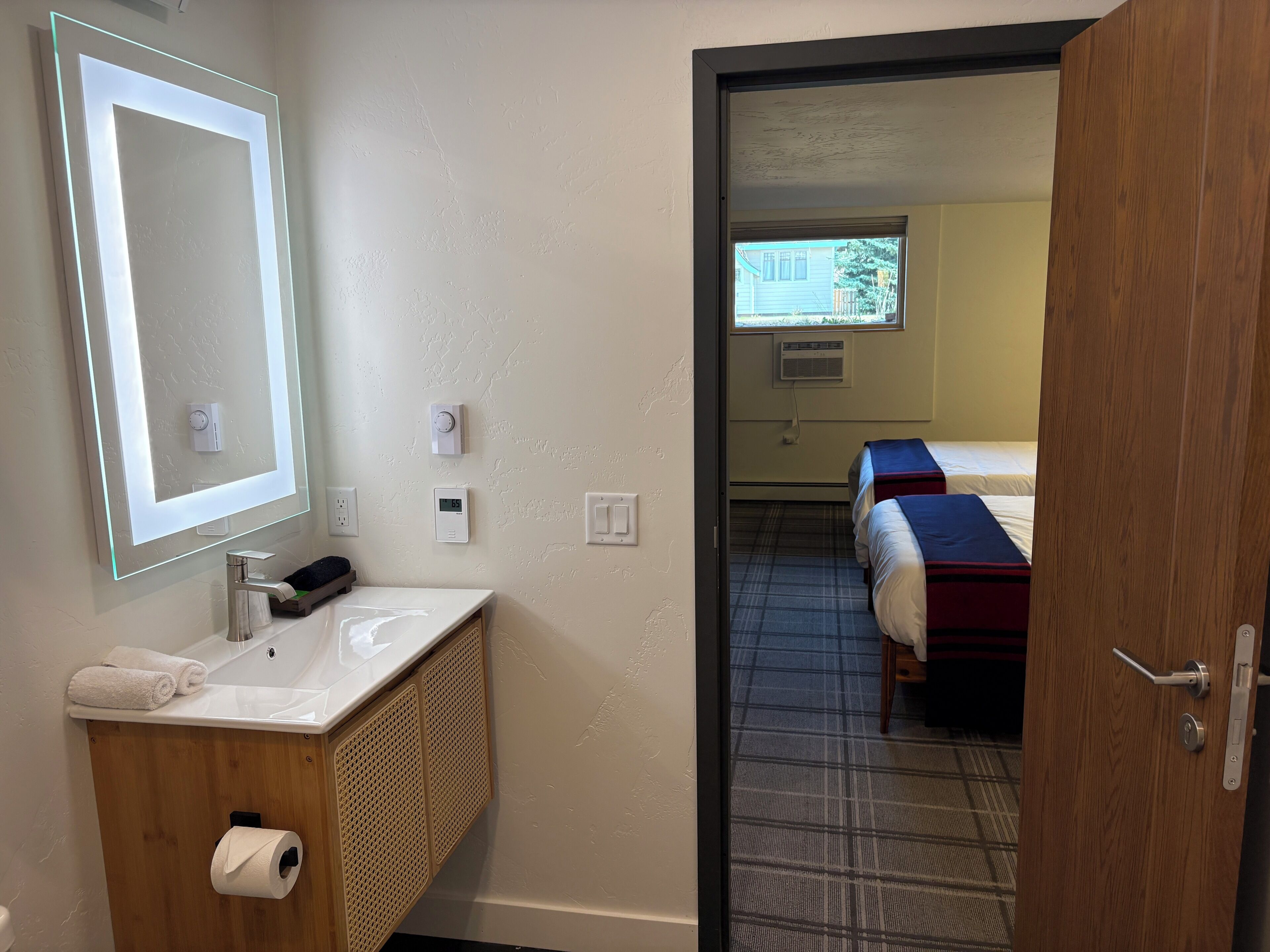 Un baño de hotel con espejo, lavamanos, dispensador de toallas y un porta papel higiénico.